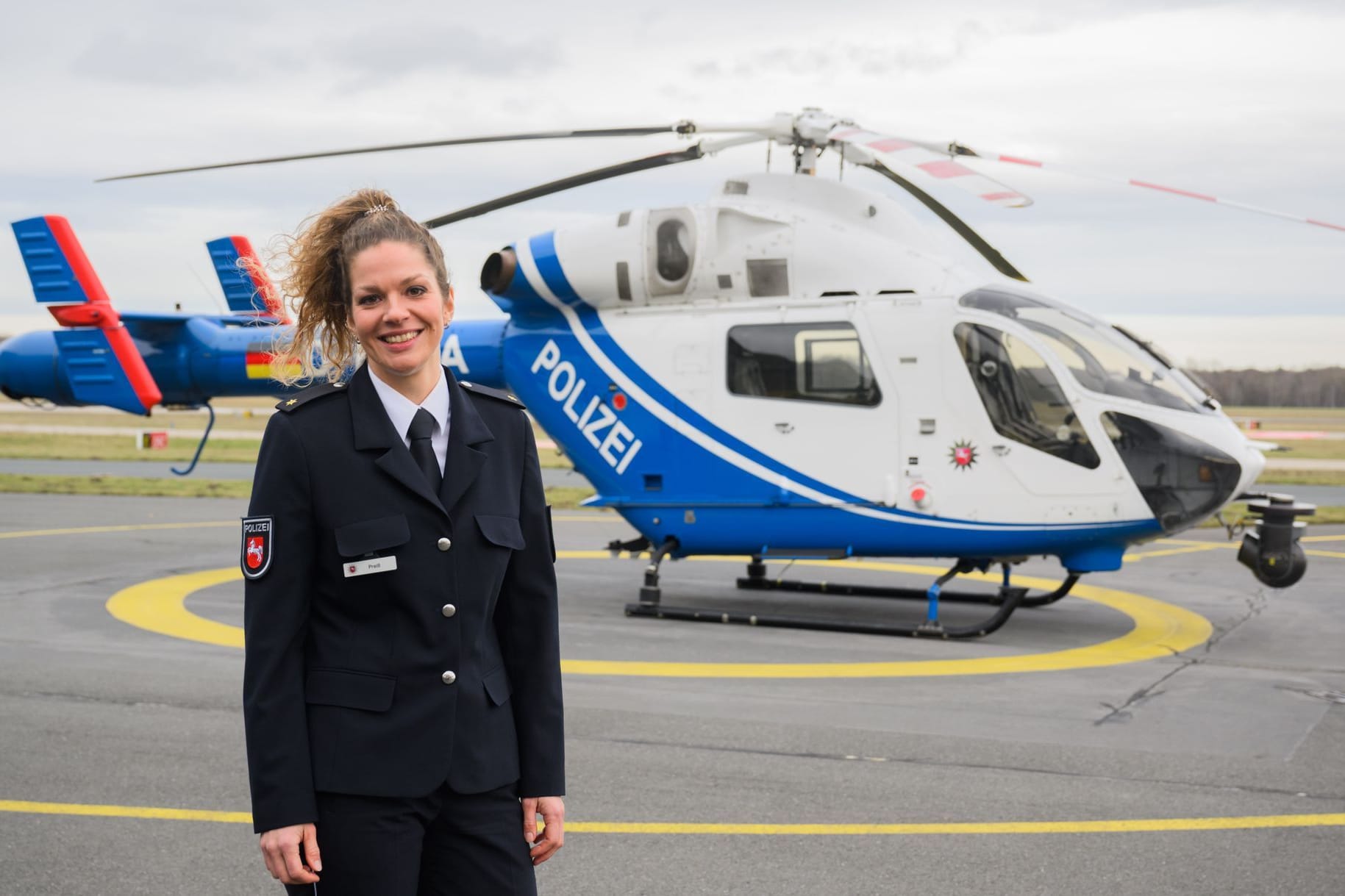 Natalie Preiß, neue Leiterin der Polizeihubschrauberstaffel Niedersachsen, steht vor einem Polizeihubschrauber MD 902 Explorer am Flughafen Hannover.