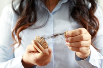 Eine Frau zieht ausgefallene Haare aus einer Bürste.