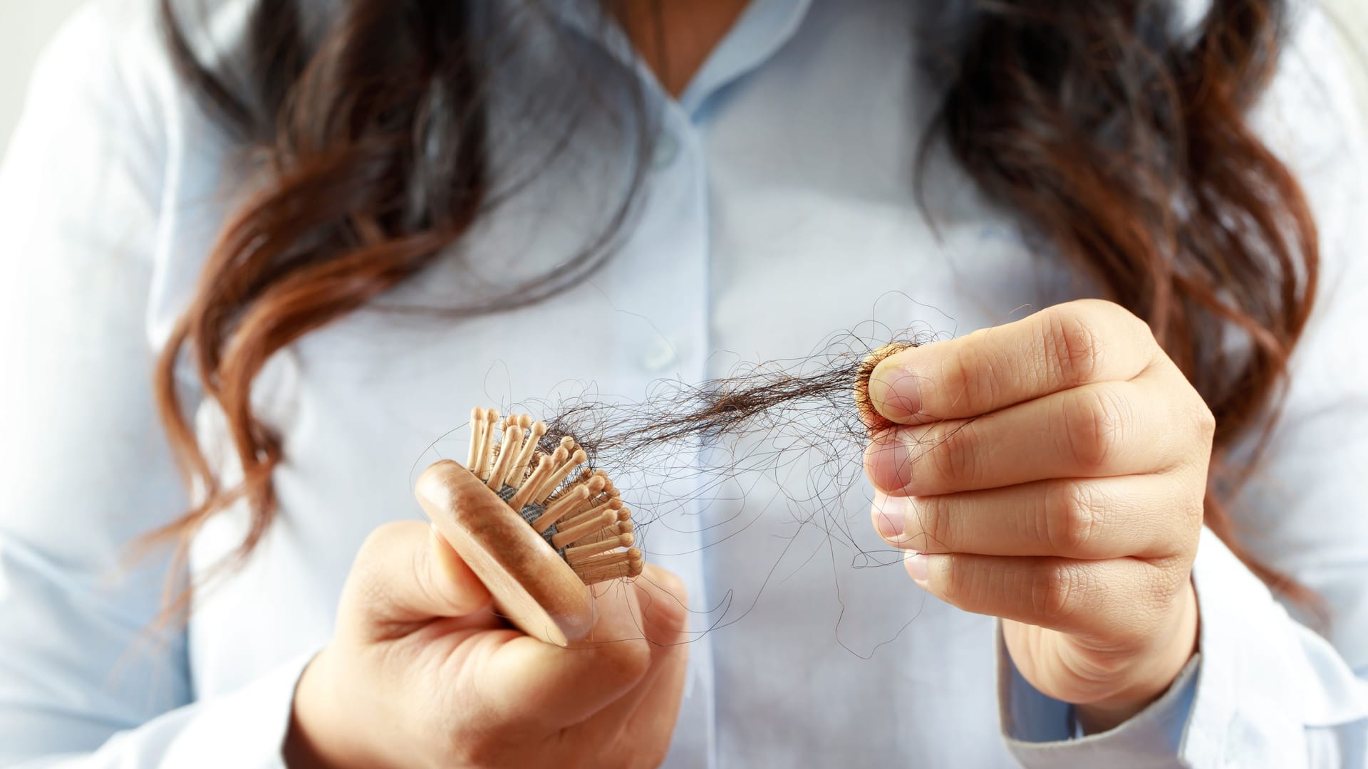 Eine Frau zieht ausgefallene Haare aus einer Bürste.