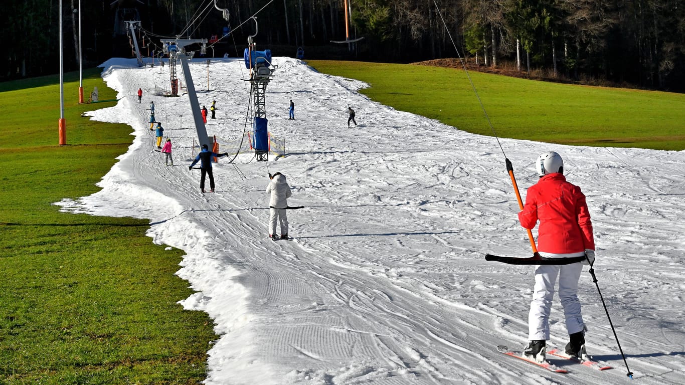 Wintersportbegeisterte bei Frühlingstemperaturen: Skifahren auf dem letzten Schneestreifen aus Kunstschnee im oberbayerischen Ruhpolding.