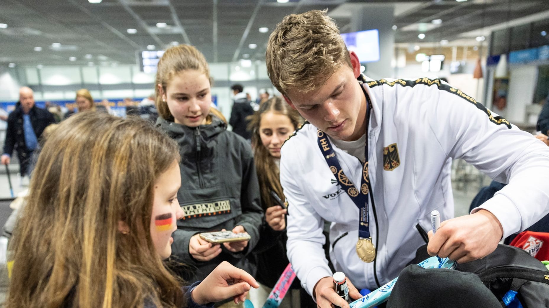 Jean-Paul Dannenberg unterschreibt auf einem Hockey-Schläger: Nach dem Sieg gegen die belgische Feldhockey Mannschaft wurde die deutsche Nationalmannschaft von Fans am Frankfurter Flughafen empfangen.