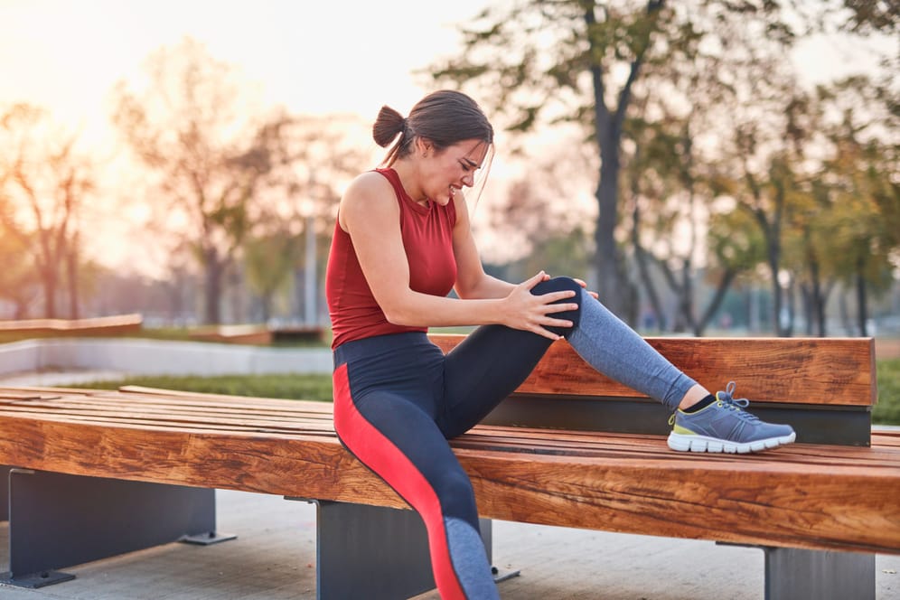 Eine Läuferin sitzt auf einer Bank und hält sich das Knie.