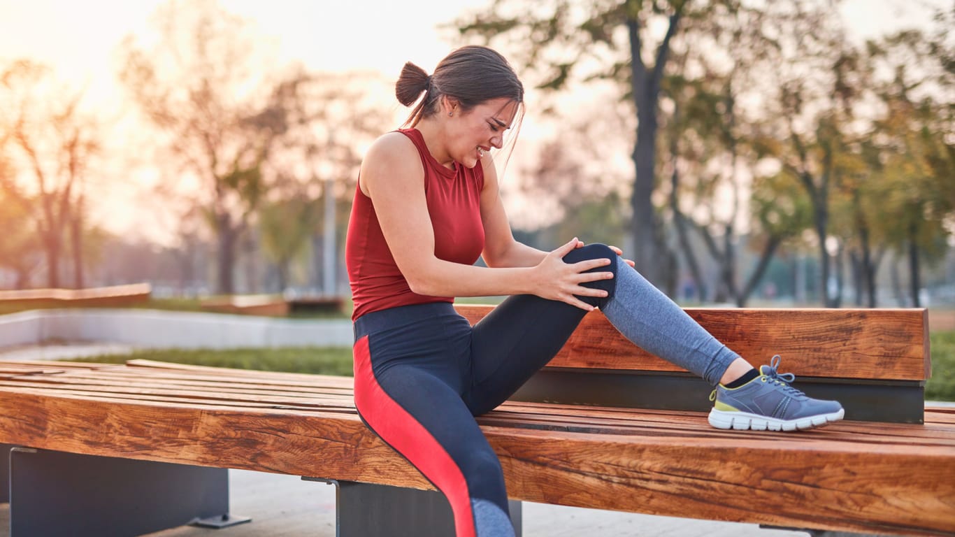 Eine Läuferin sitzt auf einer Bank und hält sich das Knie.