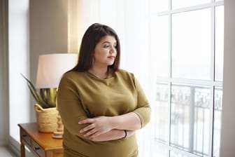 Eine Frau mit Übergewicht blickt traurig aus dem Fenster.