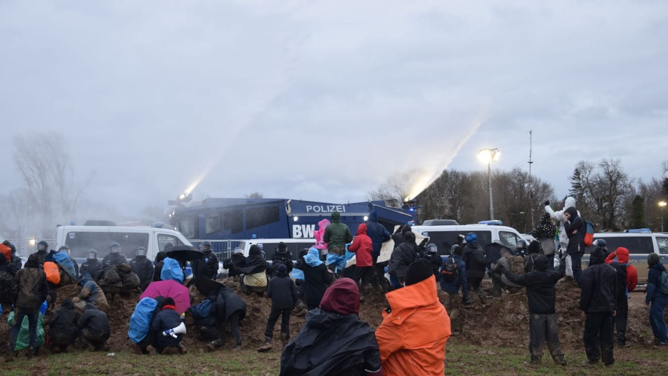 Demonstranten gehen beim Wasserwerfereinsatz in Deckung - der hat allerdings mit dem Wetter zu kämpfen.