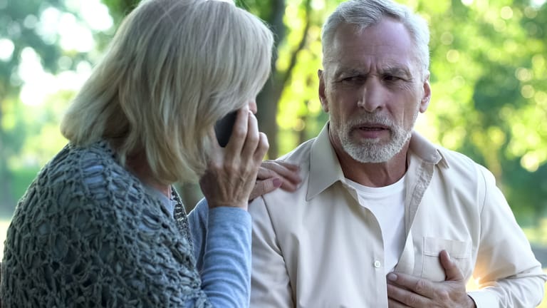 Mann mit Brustschmerzen neben telefonierender Frau