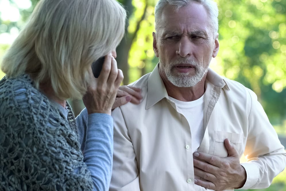 Mann mit Brustschmerzen neben telefonierender Frau