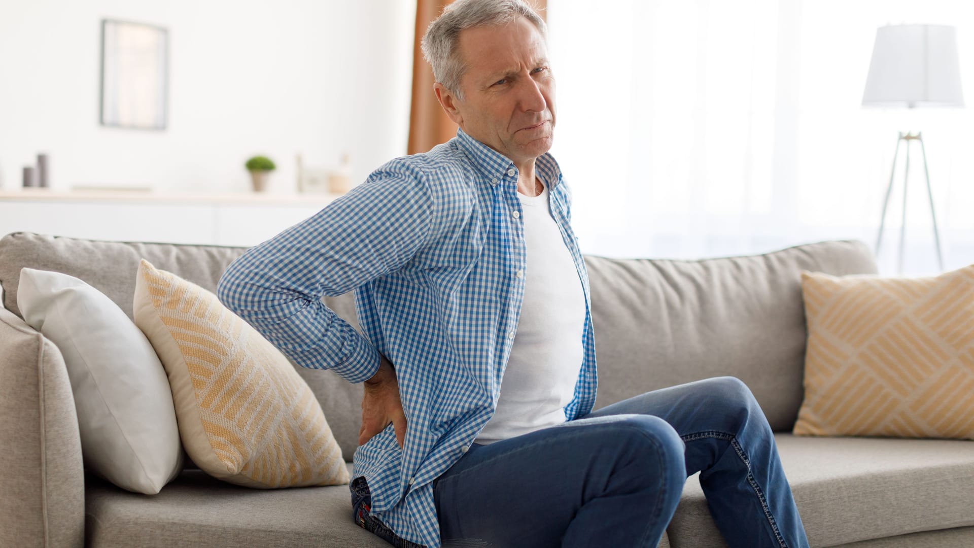 Ein Mann sitzt auf dem Sofa und fasst sich an den unteren Rücken.