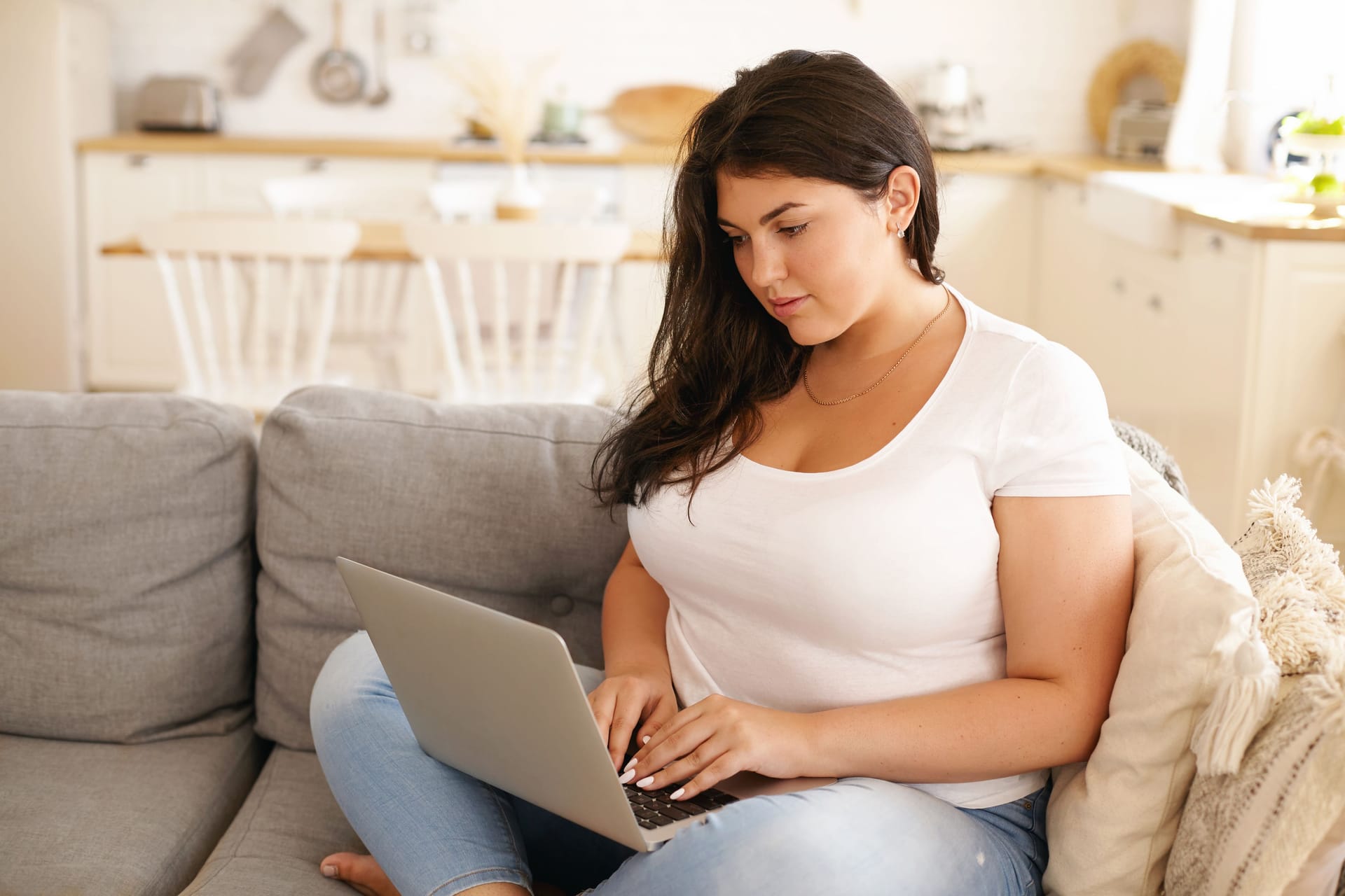 Eine Frau sitzt mit Laptop auf dem Sofa.