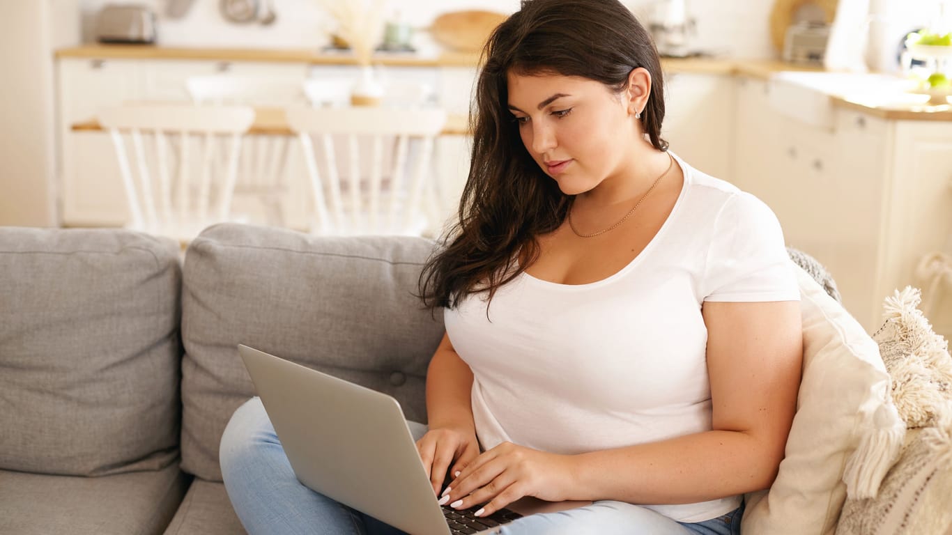 A woman sits on the sofa with a laptop.