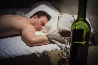 Betrunkener Mann im Bett, Weinflasche und Weinglas daneben