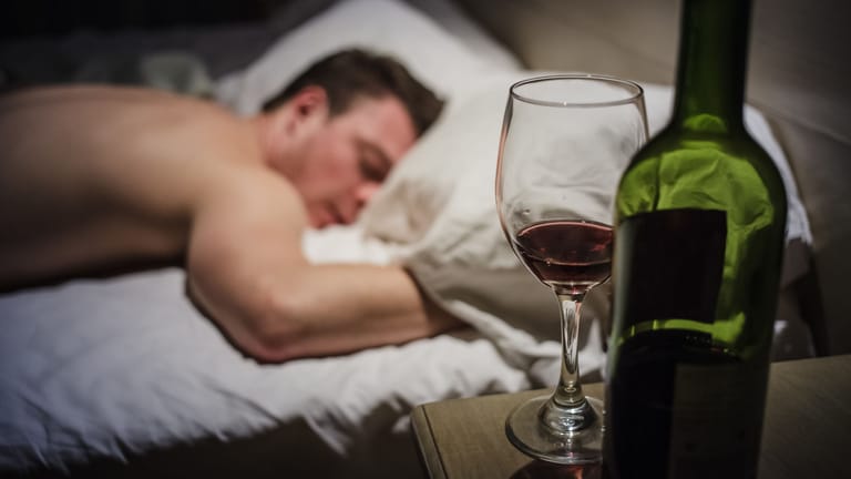 Betrunkener Mann im Bett, Weinflasche und Weinglas daneben