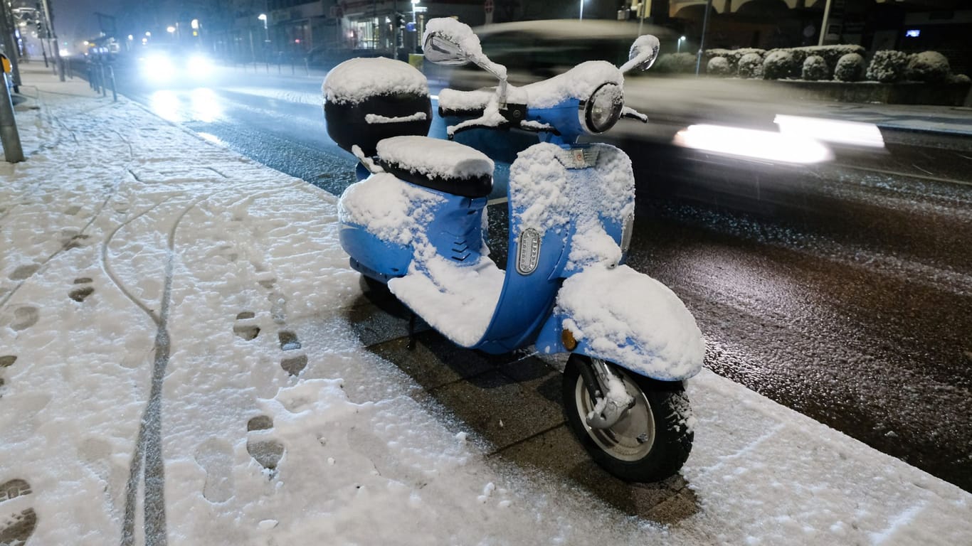 Stuttgart: Ein verschneiter Motorroller an einer Straße.