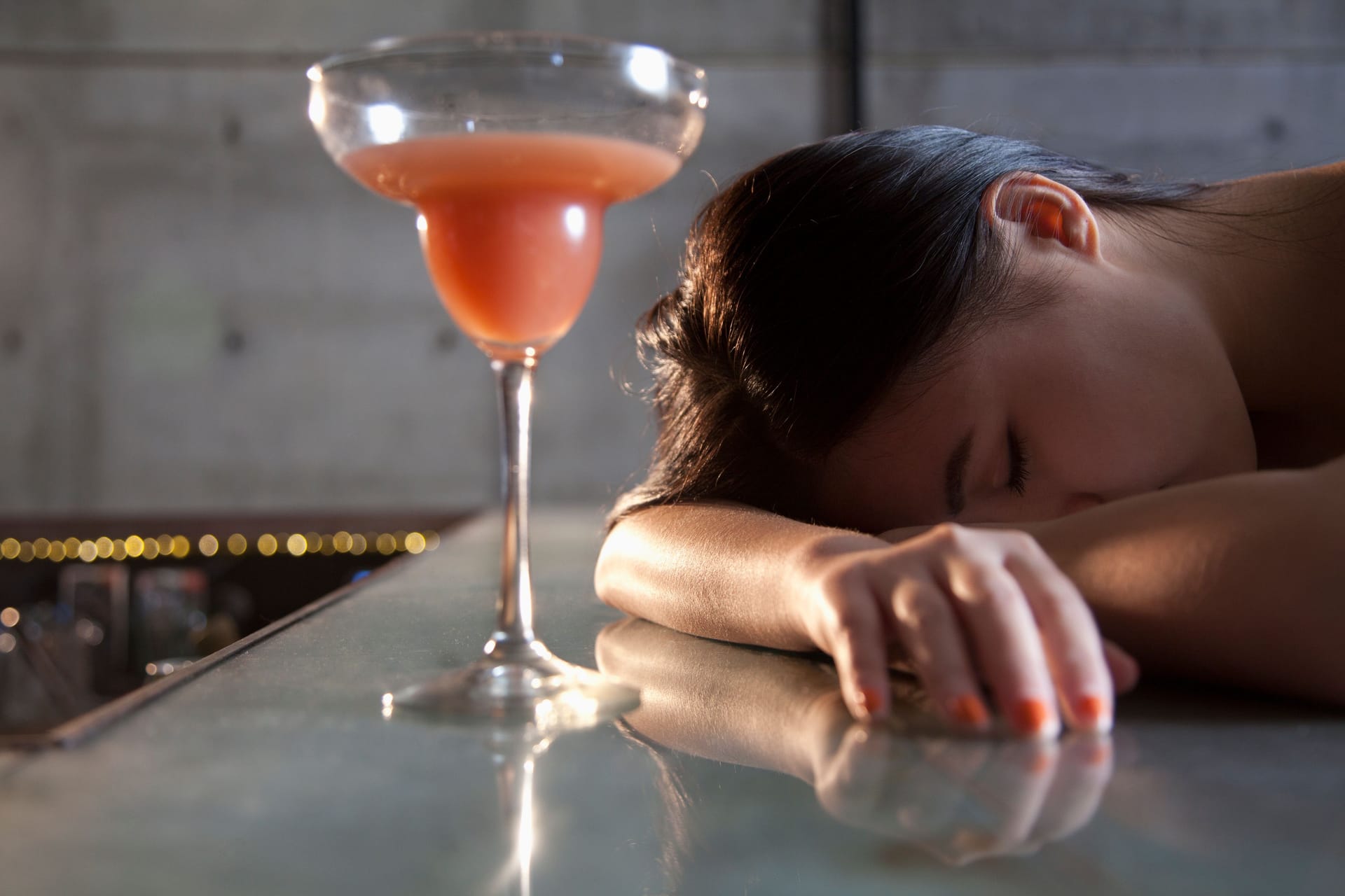 Eine Frau liegt mit dem Kopf auf der Bar, vor ihr steht ein Cocktail.