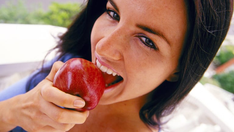 Junge Frau beißt in einen Apfel: Verbraucher sind auch ein Grund für den Einsatz von Pflanzenschutzmitteln, denn sie dienen auch der Ästhetik.