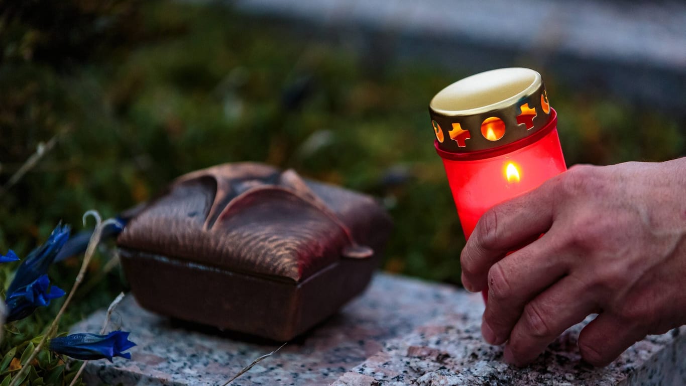 Ein Mann stellt eine Kerze auf ein Grab (Symbolbild): Stockach trauert um eine junge Mutter.
