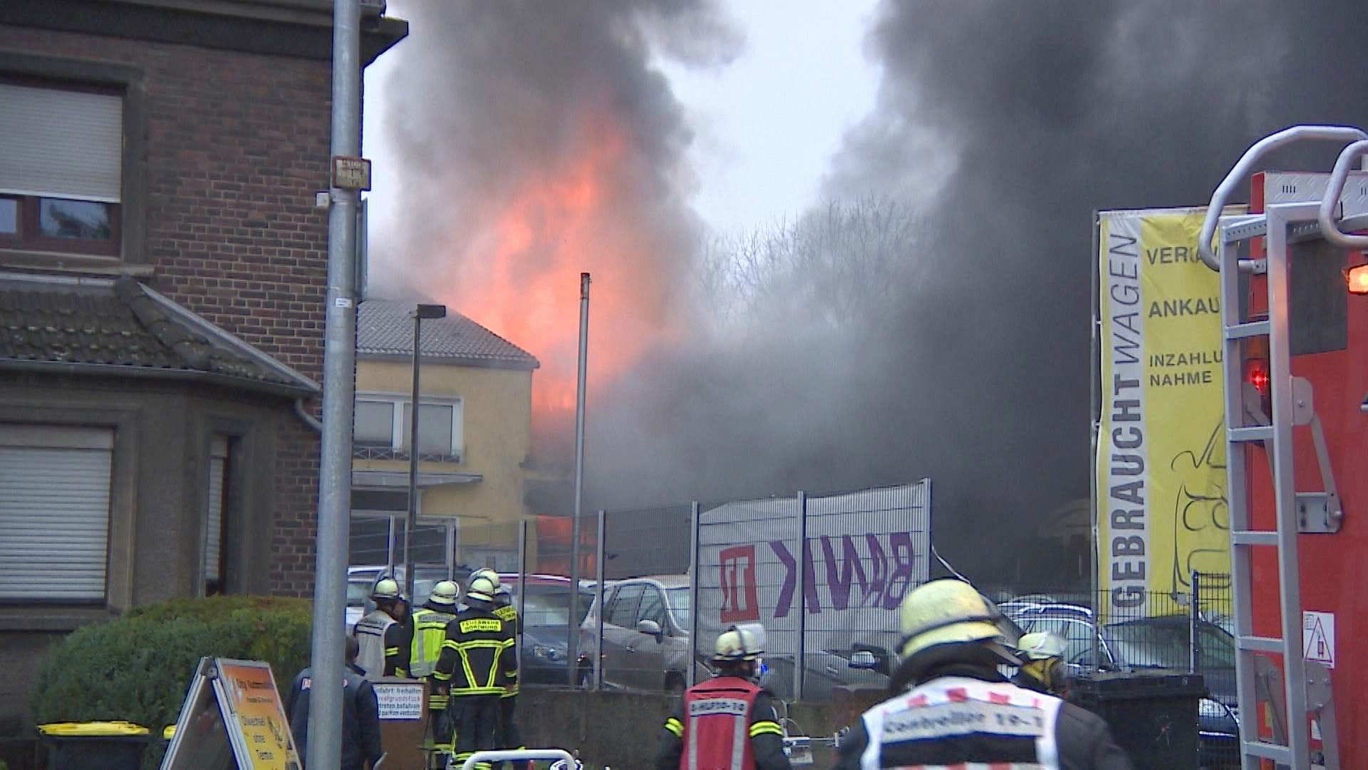 Einsatzkräfte der Feuerwehr vor den Zäunen der Kfz-Werkstatt: Der Wind erschwert die Löscharbeiten. Einsatzkräfte der Feuerwehr vor den Zäunen der Kfz-Werkstatt: Der Wind erschwert die Löscharbeiten.