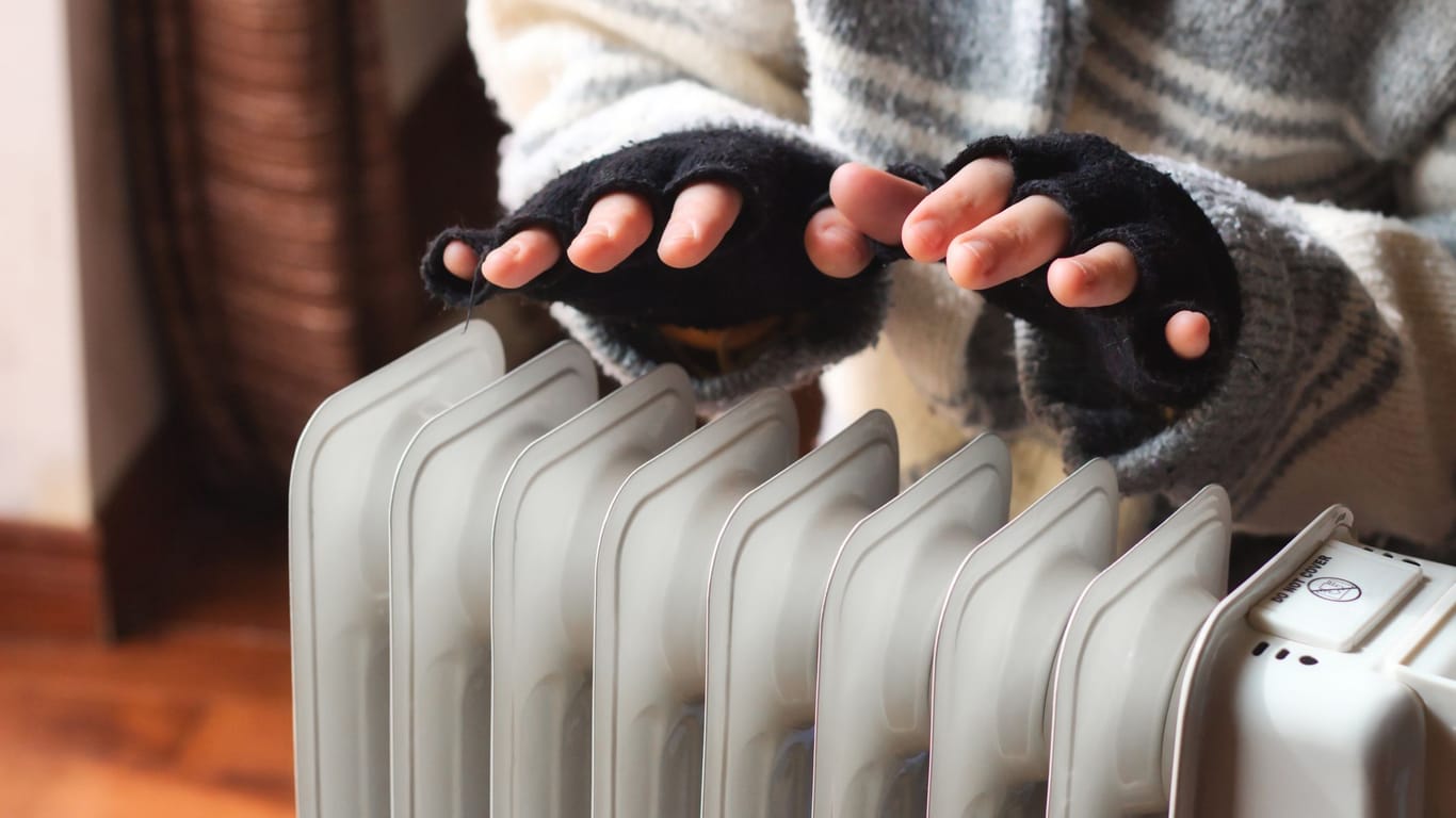 Eine Person wärmt ihre Hände über einer Heizung (Symbolbild): Studierende sollen nicht mehr lange auf ihre Energiepreispauschale warten müssen.