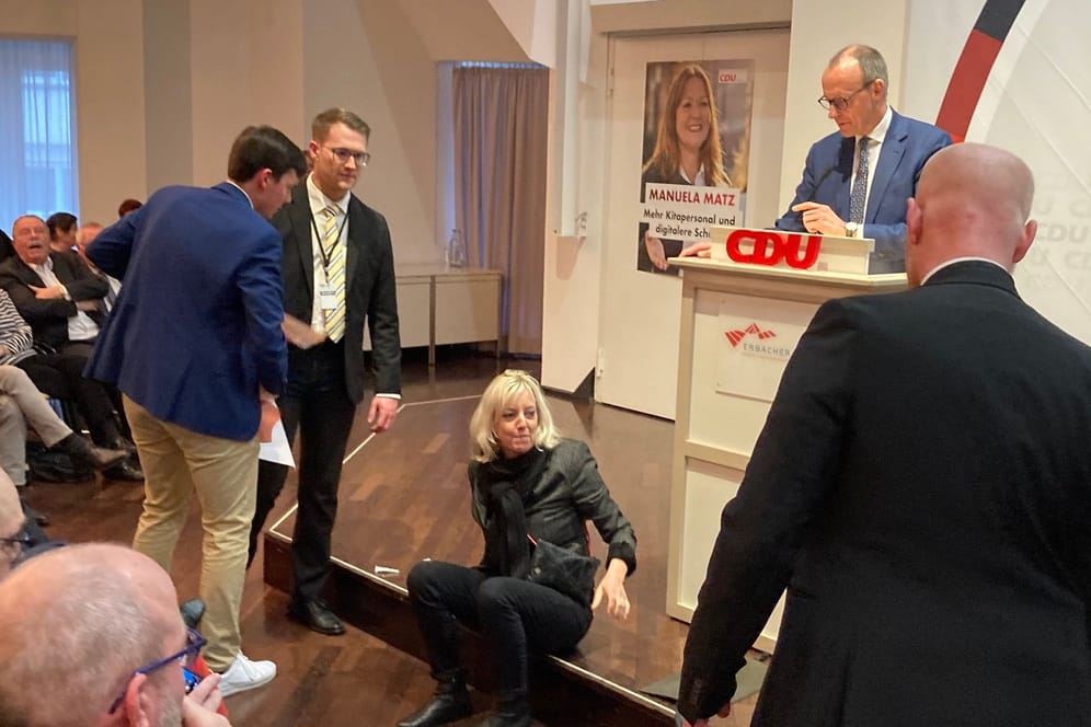 Eine von zwei Klimaschutzaktivistinnen der Letzten Generation hat sich bei einer Rede des CDU-Bundesvorsitzenden Friedrich Merz (2.v.r.) gestört und mit einer Hand auf der Bühne festgeklebt.