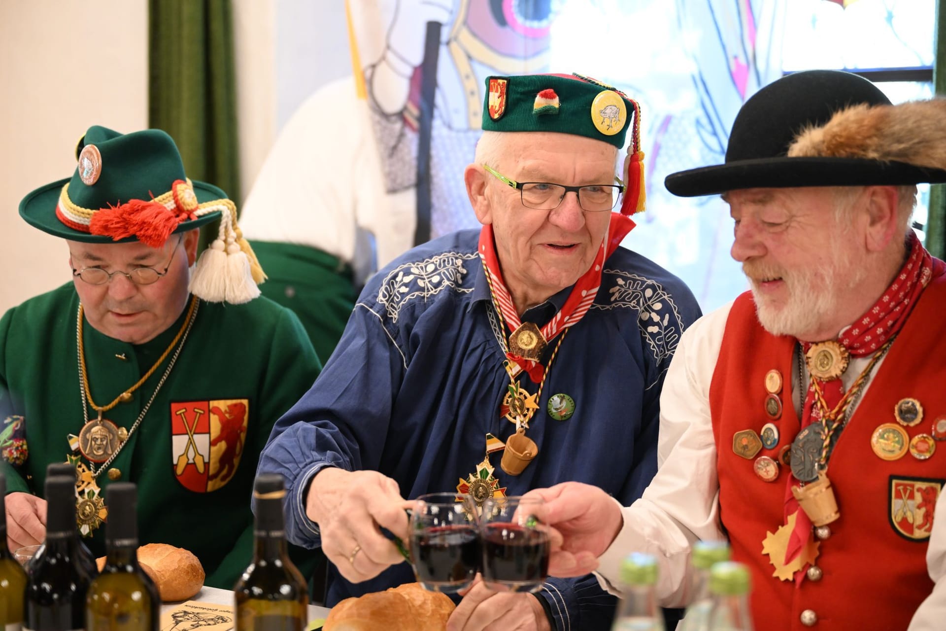 Winfried Kretschmann (Mitte) stößt am Fastnachtsdienstag mit seinen Sitznachbarn mit Wein an. Er nahm im schwäbischen Riedlingen am Froschkuttelnessen teil.