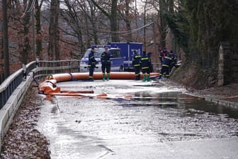 Straße am Stausee bei Dippoldiswalde: Das THW versucht mit orangenen Sperren das auslaufende Abwasser zu stauen, um es später abzupumpen.