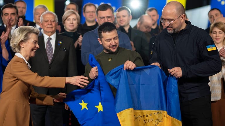 Wolodymyr Selenskyj (M.), Präsident der Ukraine, und Ursula von der Leyen (l.), Präsidentin der EU-Kommission, und Denys Schmyhal (r.), Ministerpräsident der Ukraine, halten eine europäische und eine ukrainische Standarte.
