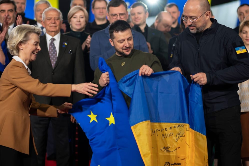 Wolodymyr Selenskyj (M.), Präsident der Ukraine, und Ursula von der Leyen (l.), Präsidentin der EU-Kommission, und Denys Schmyhal (r.), Ministerpräsident der Ukraine, halten eine europäische und eine ukrainische Standarte.