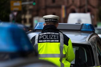 Ein Polizeibeamter steht zwischen zwei Einsatzfahrzeugen: In Troisdorf wurde eine Frau ins Gleisbett gestoßen.c