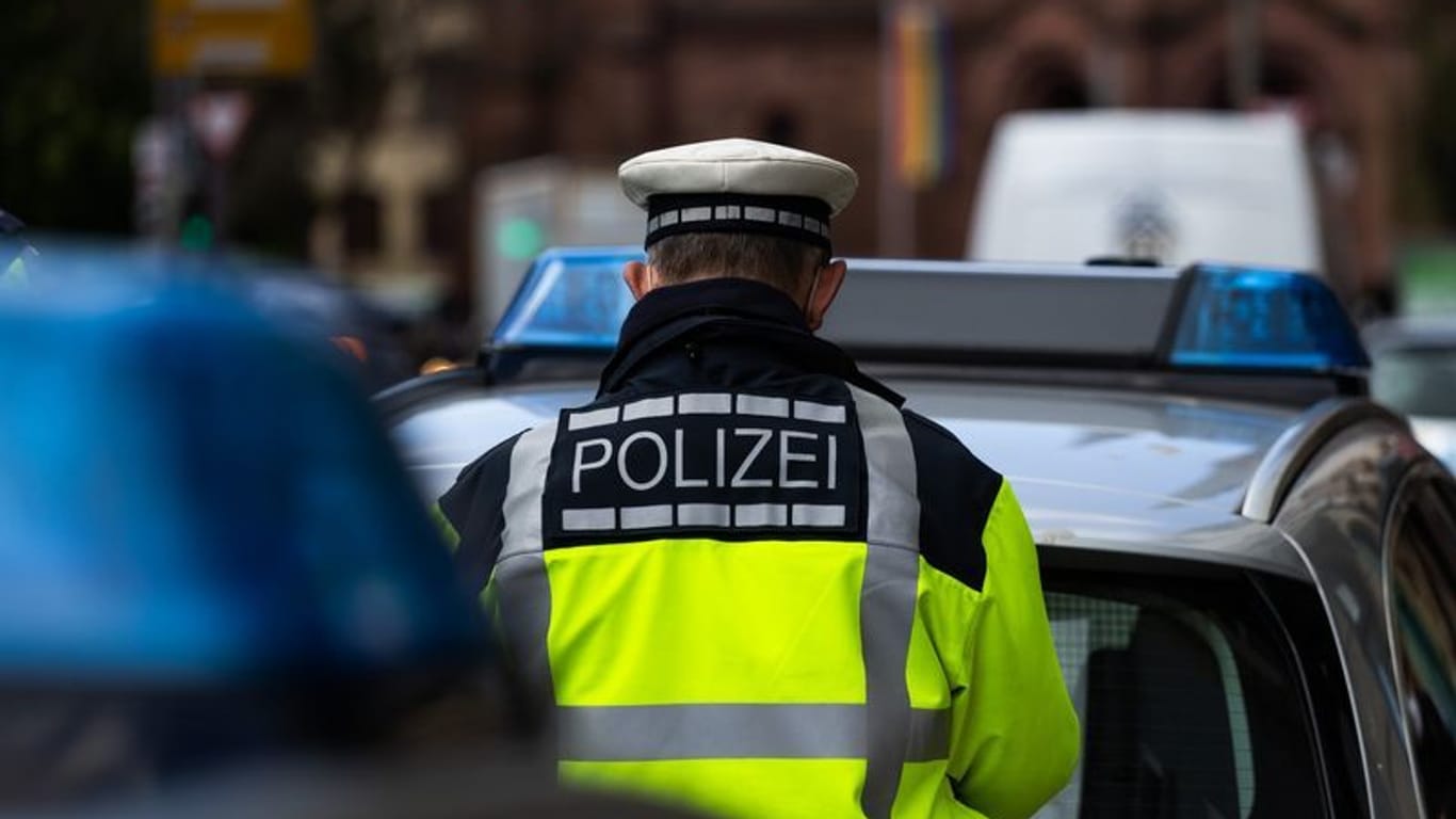 Ein Polizeibeamter steht zwischen zwei Einsatzfahrzeugen: In Troisdorf wurde eine Frau ins Gleisbett gestoßen.c