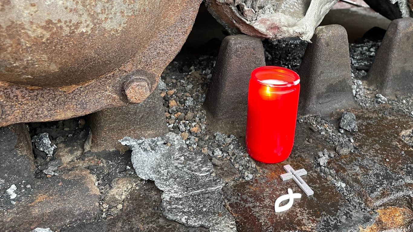 Eine Kerze, ein Kreuz und ein christliches Fischsymbol liegen in den Ketten des zerstörten Panzers.