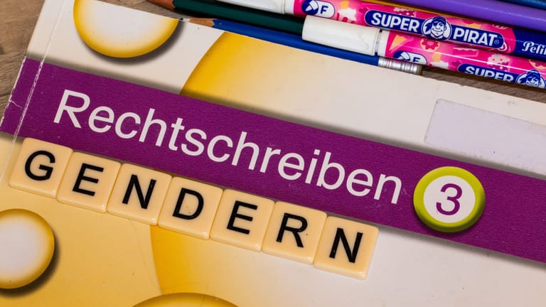 Buchstabenwürfel auf einem Grundschulbuch zeigen das Wort Gendern (Symbolbild): Geht es nach der baden-württembergischen FDP, könnte Gendern an öffentlichen Einrichtungen bald verboten sein.