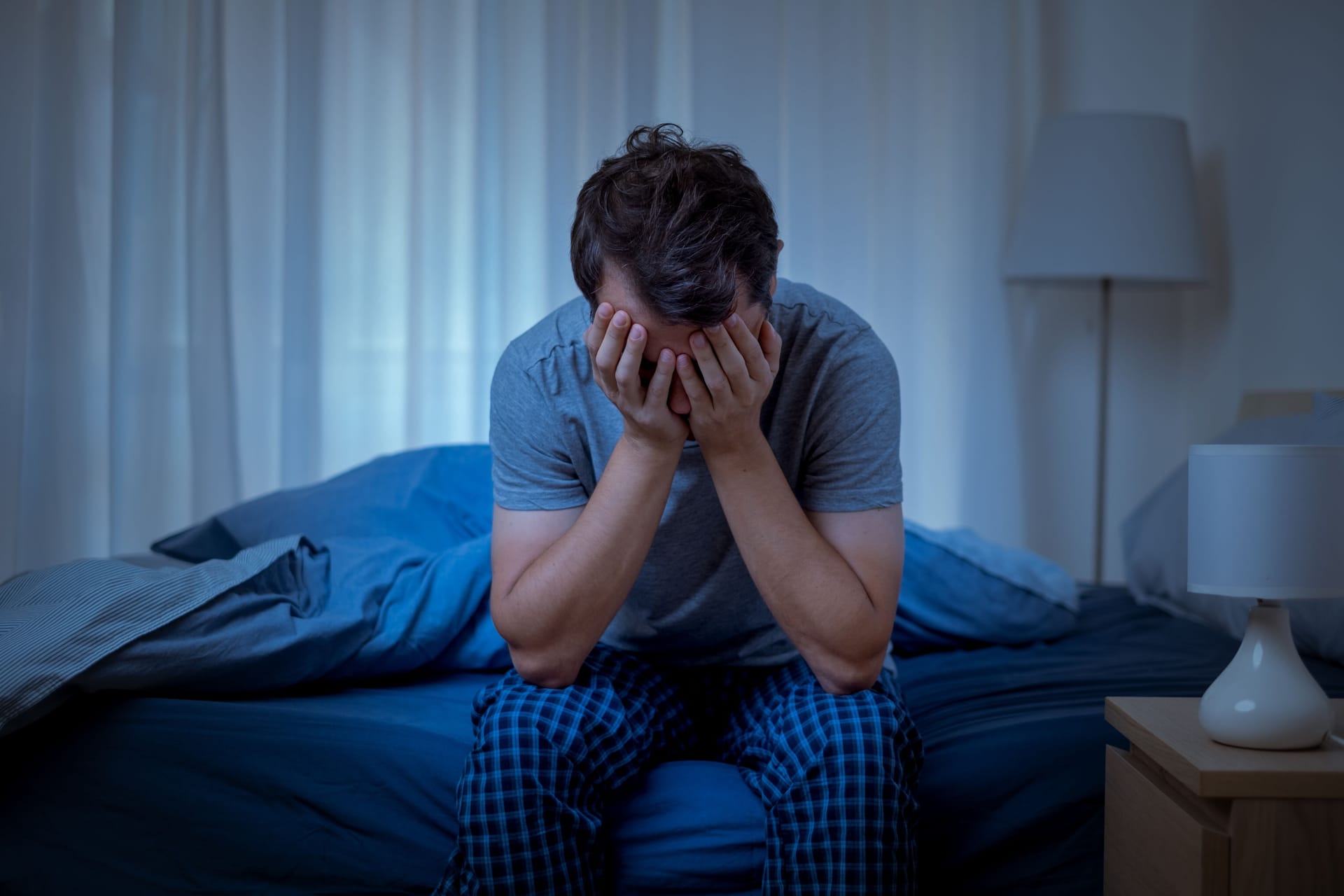 Ein Mann sitzt im Bett und hält sich die Hände vors Gesicht.