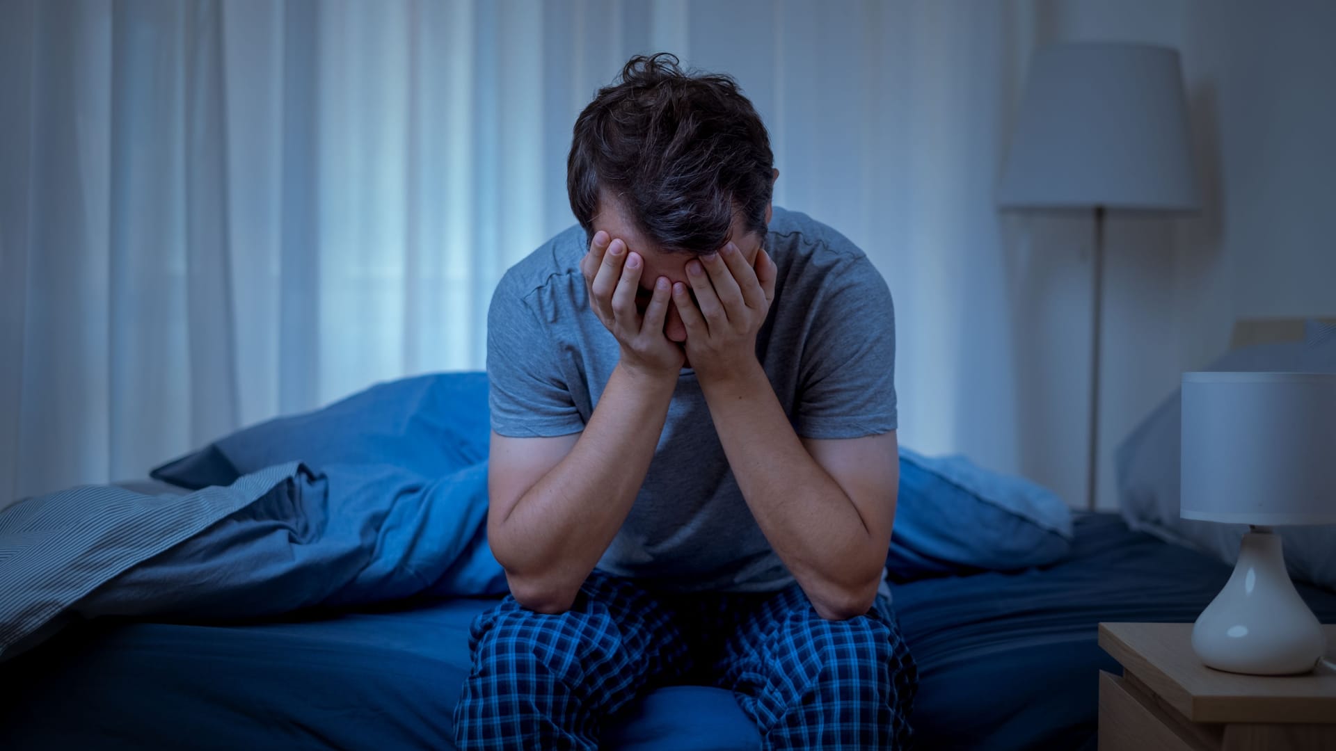 Ein Mann sitzt im Bett und hält sich die Hände vors Gesicht.