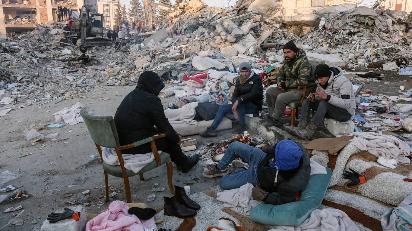 Menschen auf Stühlen und Matratzen: Viele Hinterbliebene haben Lager vor den Trümmern errichtet.