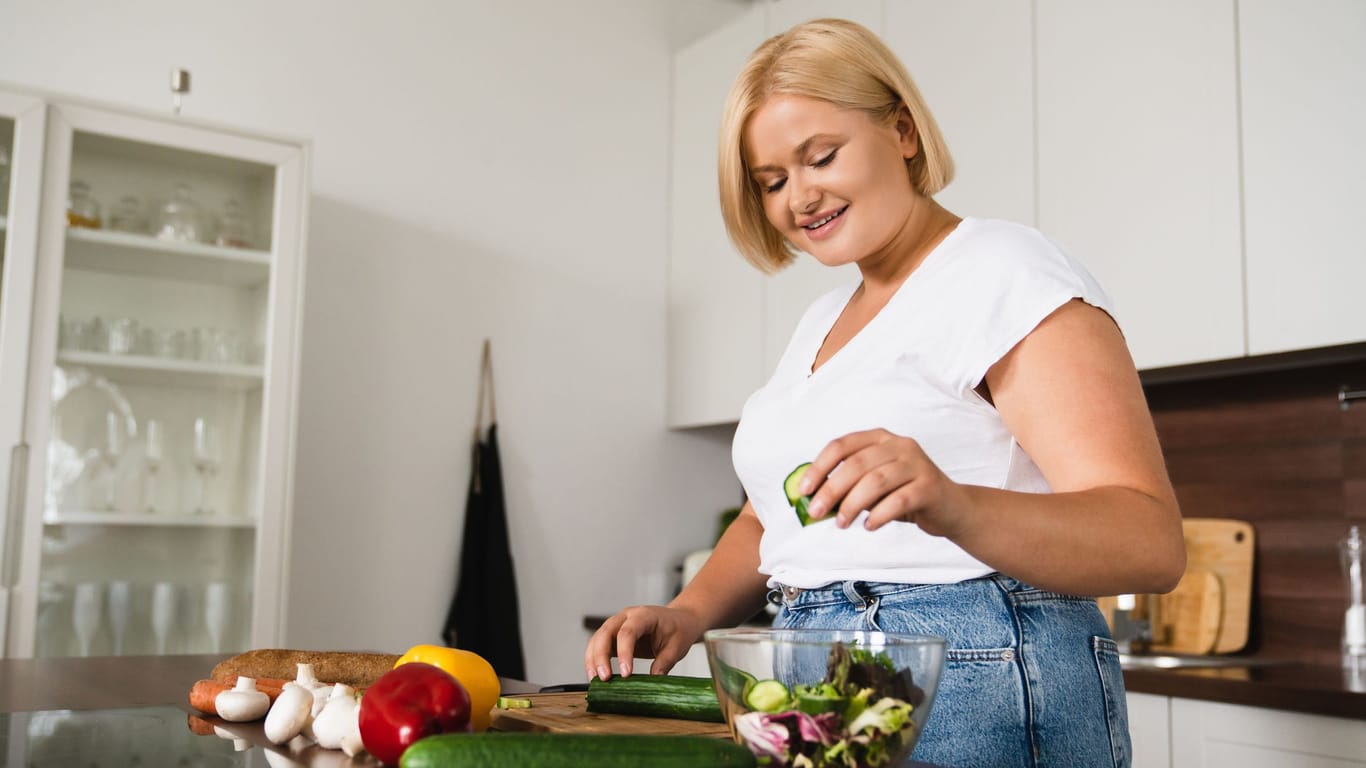 Junge, übergewichtige Frau bereitet einen Salat zu