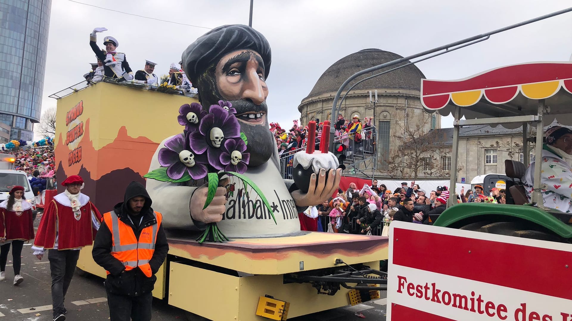 Der dritte Überraschungswagen: Der Wagen zeigt ein Taliban-Mitglied mit einem Strauß Totenkopf-Blumen und einem Kuchen in Form einer Bombe.