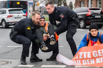 Polizisten tragen zuvor am Asphalt festgeklebte Aktivisten der Gruppierung "Letzte Generation" in Hannover von der Straße (Archivbild): Für solche Einsätze sollen die Aktivisten künftig zahlen.