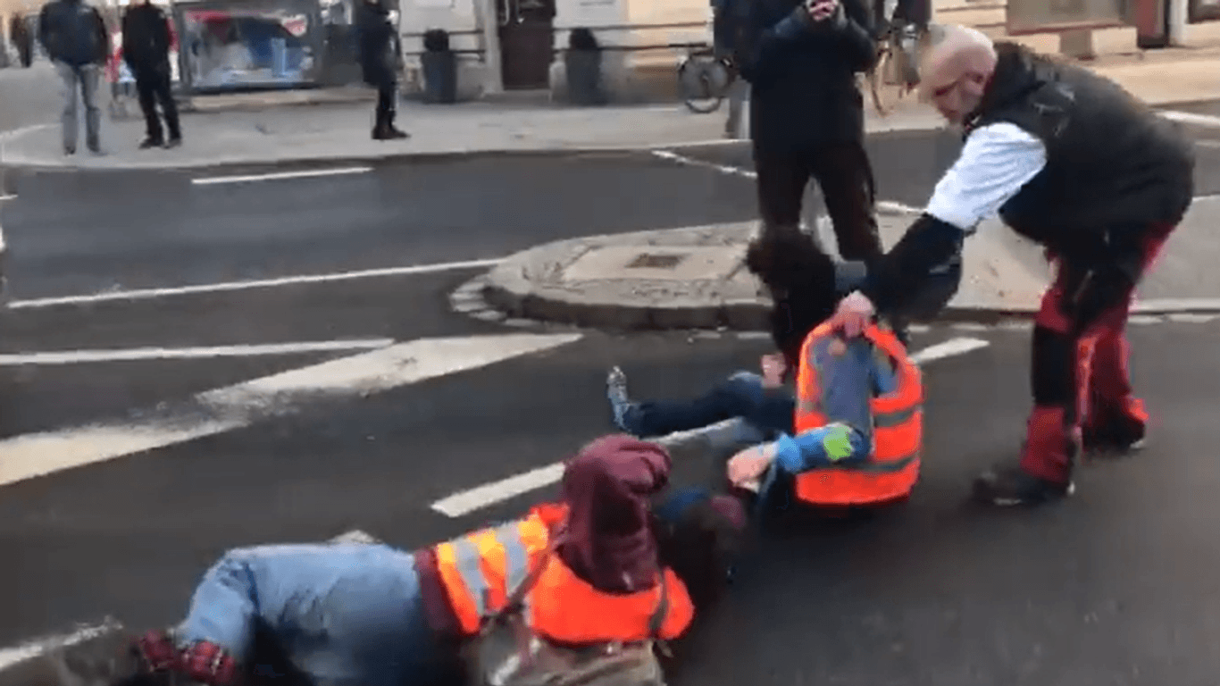 Ein Twittervideo zeigt, wie zwei Aktivisten der "Letzten Generation" am Schillerplatz von der Straße gezogen werden.