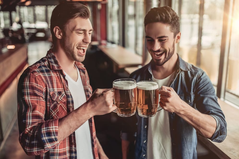 Zwei junge Männer stoßen mit einem Bier an.