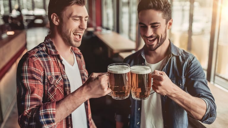 Zwei junge Männer stoßen mit einem Bier an.