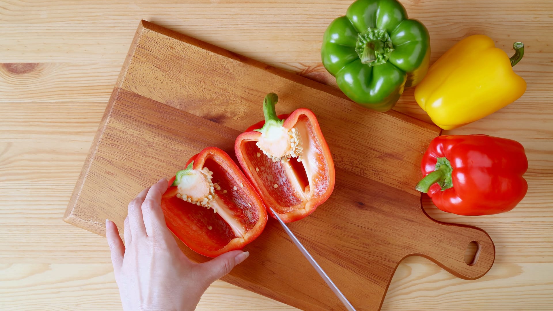 Jemand schneidet Paprika auf einem Holzbrett.