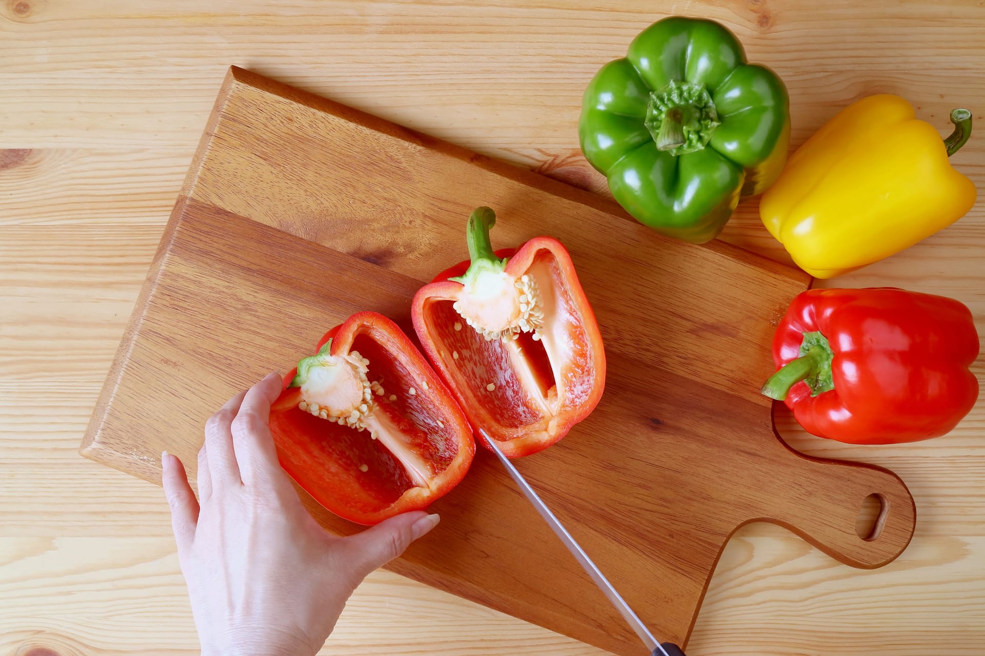 Jemand schneidet Paprika auf einem Holzbrett.