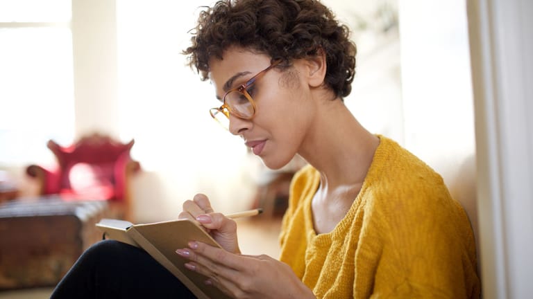 Eine Frau schreibt in ein Notizbuch (Symbolbild): Ob am Computer, per App oder klassisch auf Papier – wie Sie ein Haushaltsbuch führen, ist Ihnen überlassen.