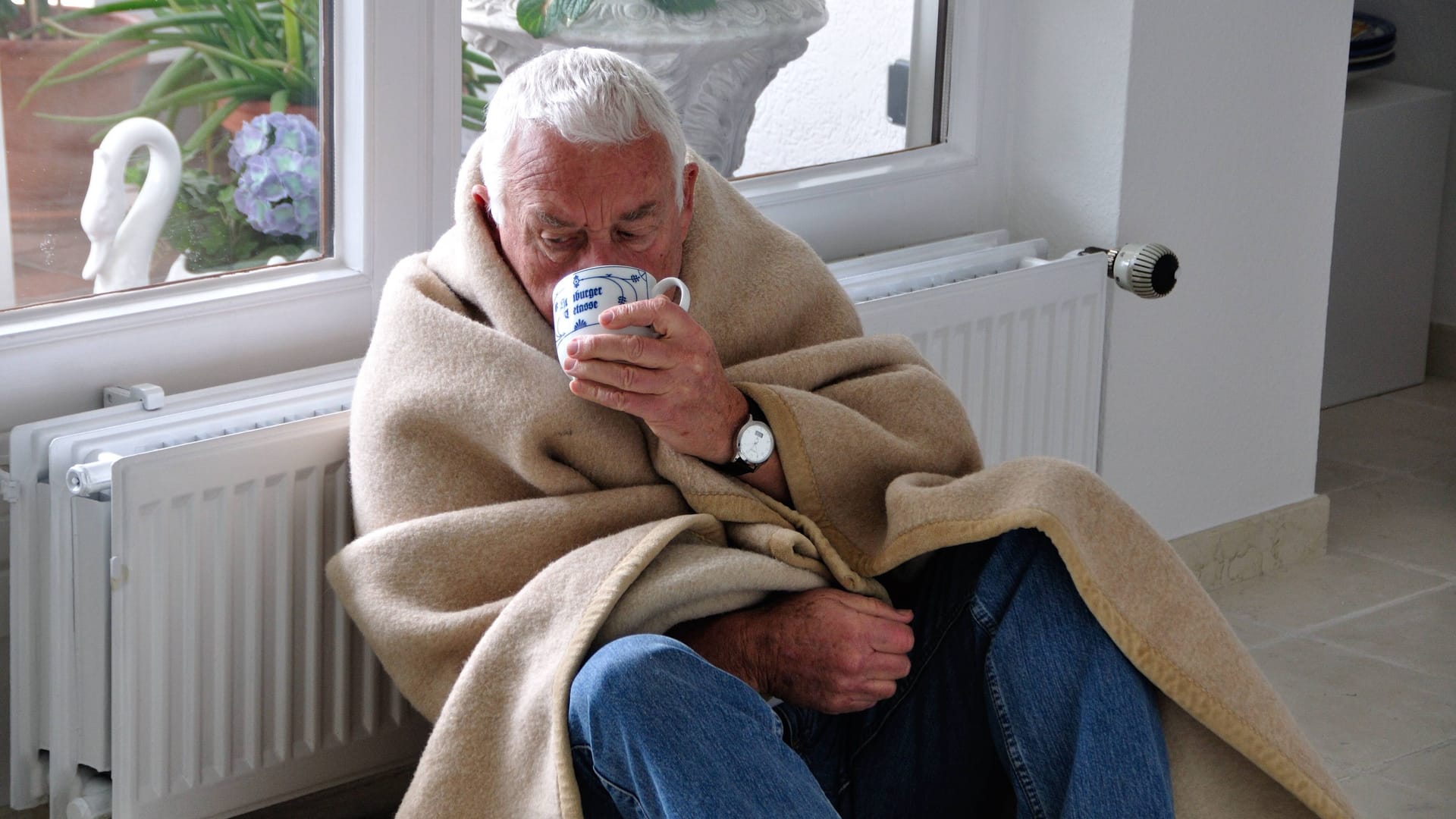 Ein Mann sitzt mit einer Tasse Tee und Decke frierend vor einer Heizung (Symbolbild): Eine Woche lang saßen die Bewohner eines Wohnkomplexes in Hannover in der Kälte. Ein Mann sitzt mit einer Tasse Tee und Decke frierend vor einer Heizung (Symbolbild): Eine Woche lang saßen die Bewohner eines Wohnkomplexes in Hannover in der Kälte.