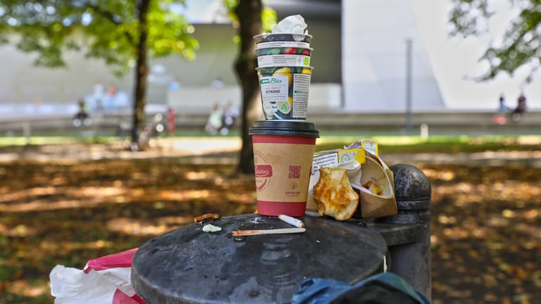 Ein Einweg-Kaffeebecher auf einem überfüllten Mülleimer: