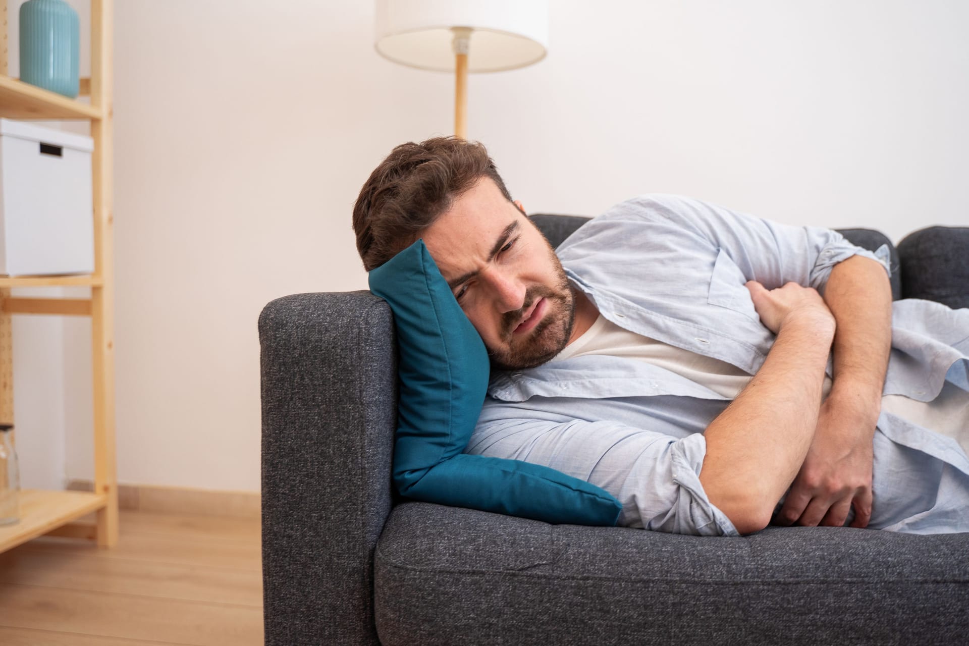 Ein Mann liegt auf dem Sofa und hält sich den Bauch.