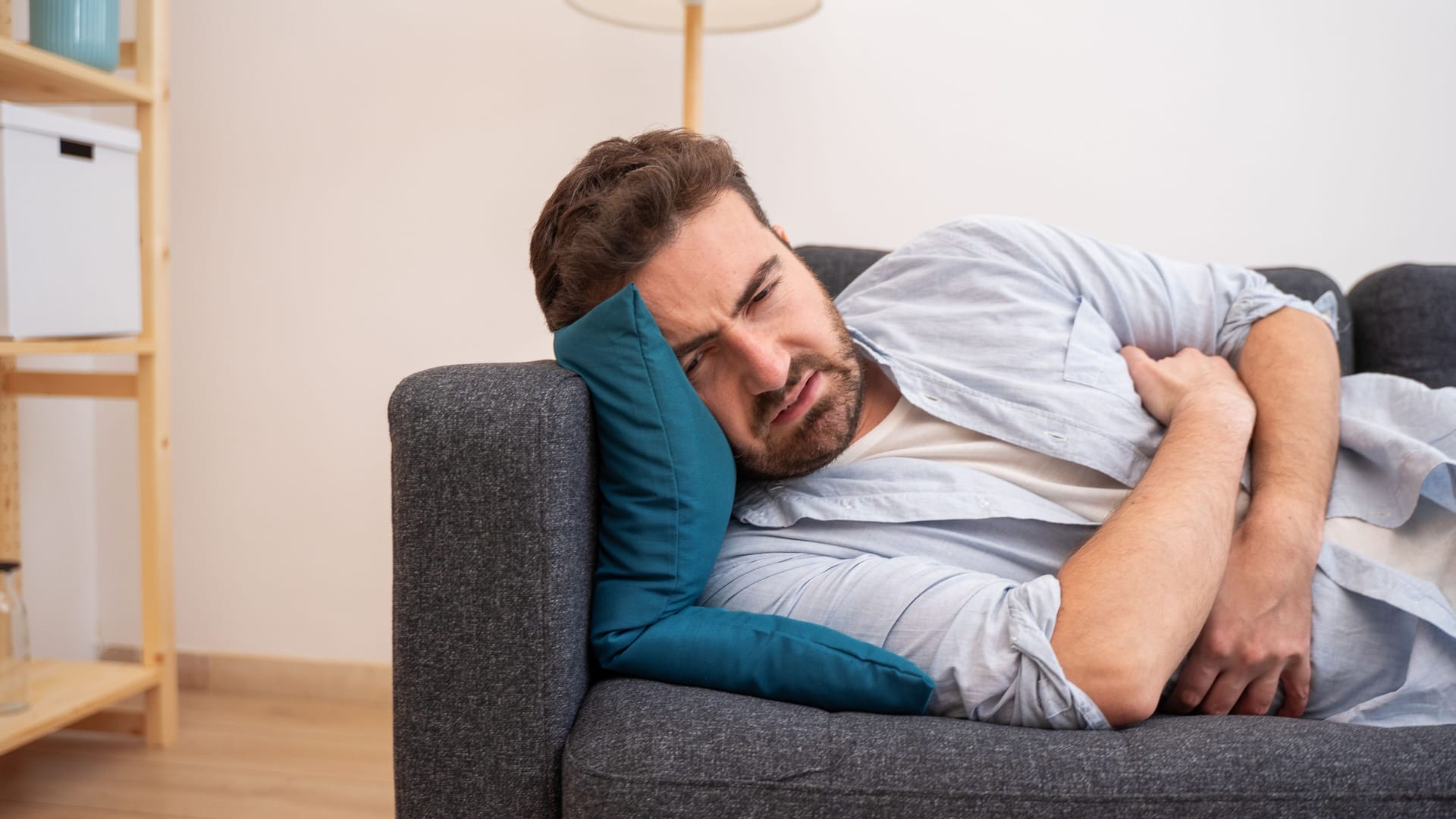 Ein Mann liegt auf dem Sofa und hält sich den Bauch.