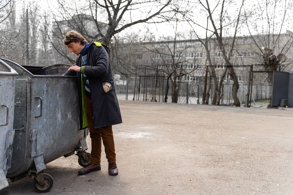 Ein junger Mann schaut in eine Mülltonne: Auf der Suche nach Schätzen scheuen einige nicht davor, in fremde Mülltonnen zu schauen. (Symbolbild)