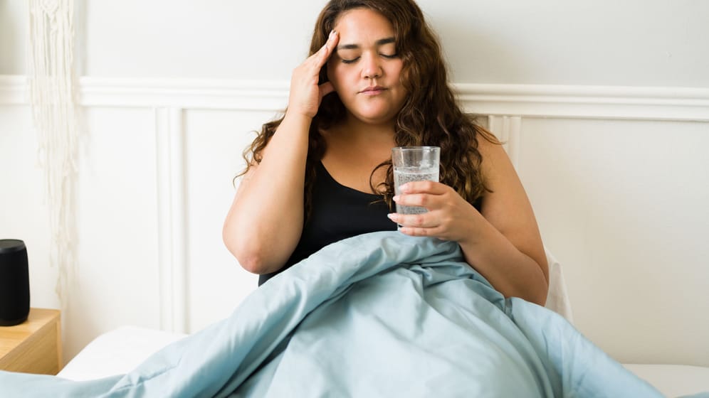 Eine junge Frau mit Kopfweh trinkt ein Glas Wasser.