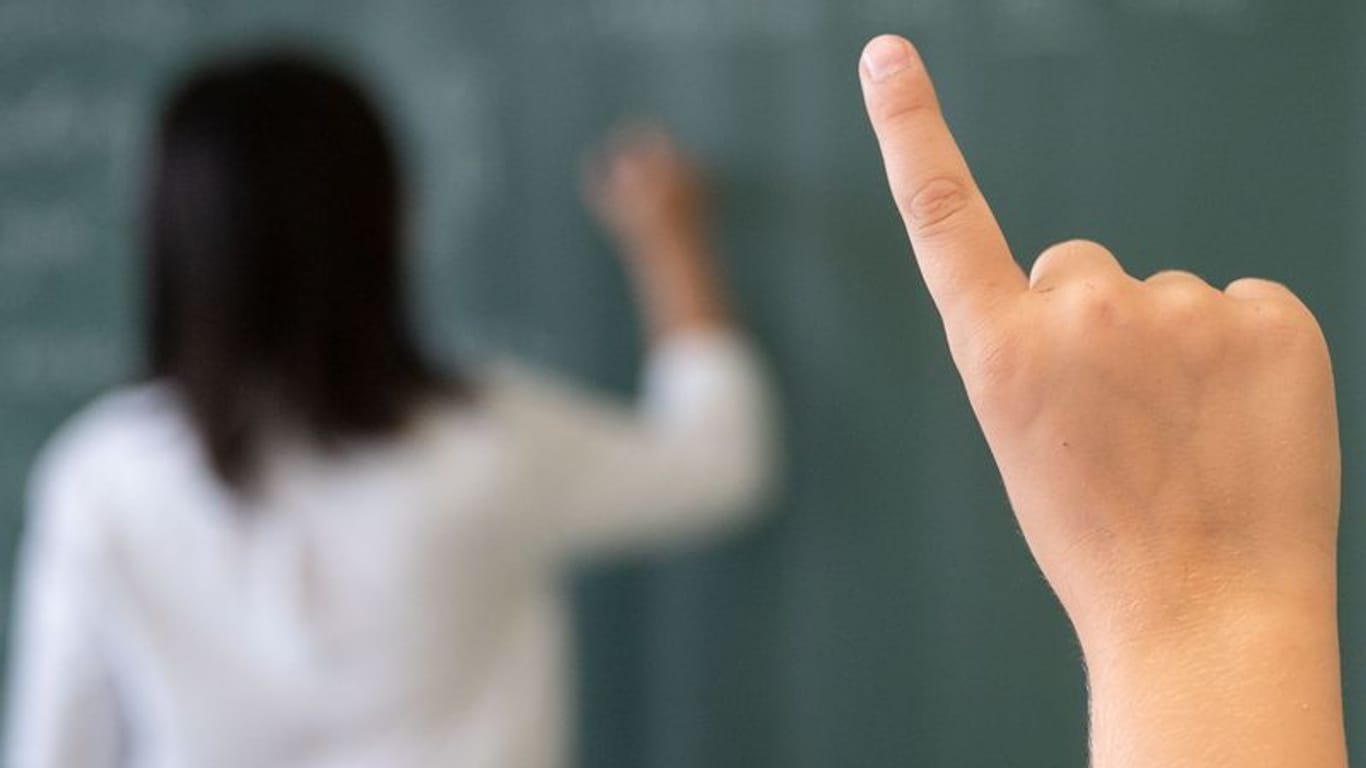 Ein Schüler meldet sich, während die Lehrerin an die Tafel schreibt (Symbolfoto): Besonders Frauen reduzieren häufig ihre Arbeitszeit.